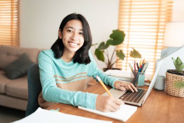 Mutlu Asyalı kız gülümsemesi, Asyalı öğrenci evde bilgisayardan öğreniyor. Kameraya bakan kadın portresi