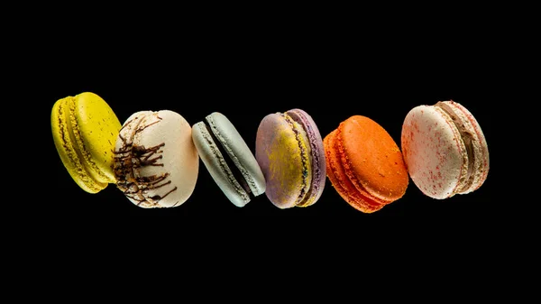 Siyah zemin üzerinde izole edilmiş uçan renkli badem kurabiyeleri ya da pastalar havada asılı duruyor. Tatlı ve renkli tatlı Kopya Uzay Renkli Fransız kurabiyeleri