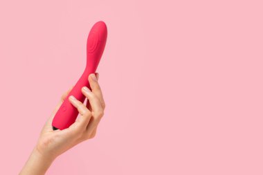 Female hand is holding pink dildo on a pink background. Pink vaginal vibrator in the hand of a woman. Sex toys. Place for text. Sex shop concept. Copy space Shop for adults.