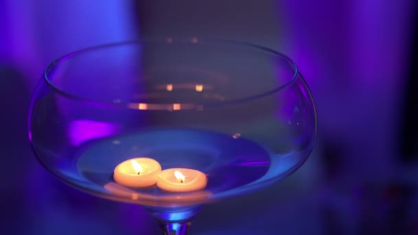Velas flotando en un jarrón de vidrio en la noche sobre una iluminación de fondo violeta — Vídeo de stock