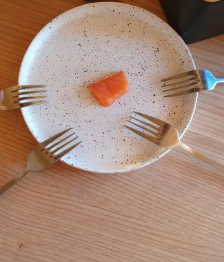 Küçük bir parça kırmızı balık bir tabağın üzerinde yatıyor ve etrafında dört tane çatal bulunuyor. Basitliğe vurgu yapan şık bir kompozisyon. Yemek pişirme, sağlıklı beslenme ve modern tasarım temaları için.