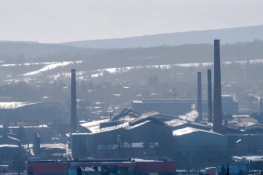 Ostrowiec Swietokrzyski şehir binaları arasında yükselen çok sayıda uzun bacası olan tarihi çelik fabrikalarına ev sahipliği yapıyor. Manzara kışın, Kutsal Haç Dağları 'nın karlı, sisli zeminine karşı kuruludur. Sanayi kompleksi bir karışım sergiliyor .