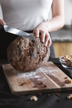 Ahşap bir tahtada ceviz ve kuru üzümle dolu çavdar ekmeğini dilimleyen kadın, zanaatkar ev yapımı ekmeklerini gösteriyor..