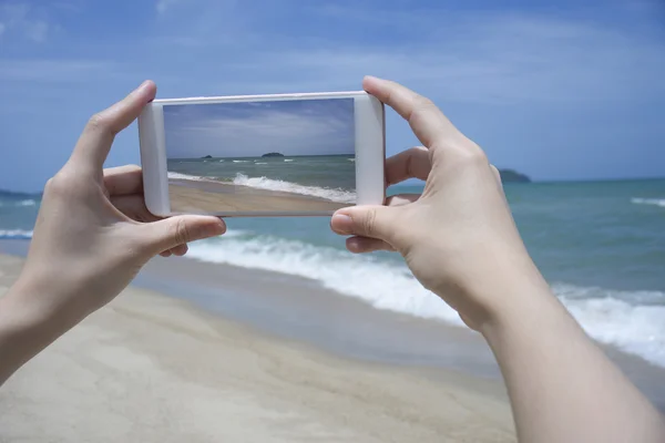 Close up of woman's hand holding smartphone, mobile, smart phone over blurred beautiful blue sea to take a photo of the sea