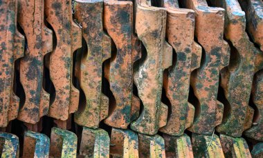 Yıpranmış doku ve yosunlara sahip eski terracotta çatı kiremitleri yığını, bir inşaat veya restorasyon ortamında kırsal yapı malzemelerini gösteriyor