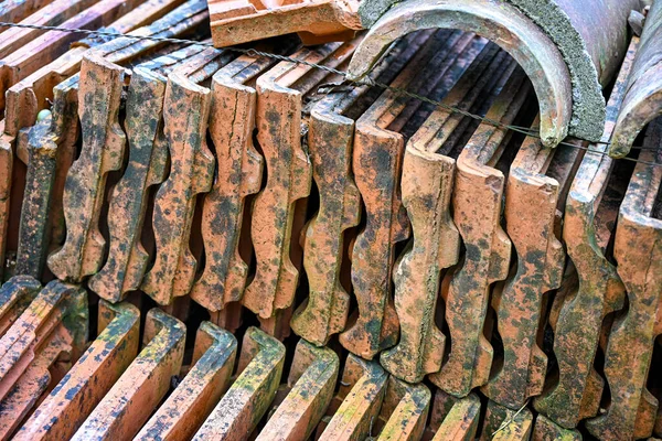 Yıpranmış doku ve yosunlara sahip eski terracotta çatı kiremitleri yığını, bir inşaat veya restorasyon ortamında kırsal yapı malzemelerini gösteriyor
