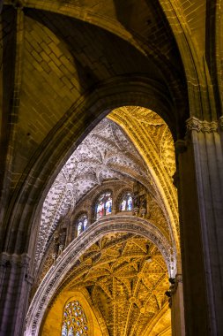 Karmaşık Gotik kemerleri ve vitray pencereleri olan Sevilla Katedrali 'nin içi altın ışıkla aydınlatılmış, inancı, zanaatkarlığı ve kutsal sanatın ihtişamını ifade eden