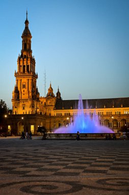 Seville 'deki Plaza de Espana cephesinin akşam manzarası aydınlık çeşme ve kuleyle, lamba direkleriyle, mimari görkem, sıcak ışık ve huzurlu Endülüs atmosferiyle
