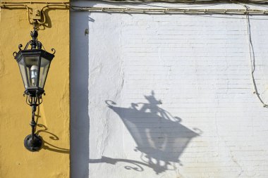 Seville 'de sarı ve beyaz bir duvara işlenmiş zarif bir lamba, yumuşak bir gölge bırakıyor, Akdeniz sadeliği, gelenek ve günlük tasarımın şiirselliğini yansıtıyor.