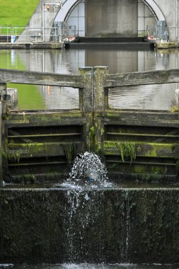 Su, İskoçya 'da yosunlu ahşap yapılar bulunan bir kanal kilit kapısından akıyor.