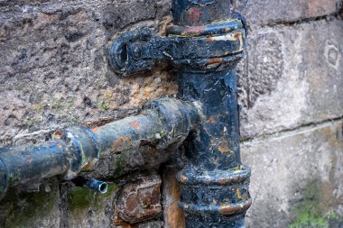 Taş duvardaki yıpranmış metal boru, yaşı, aşınma, doku ve kentsel altyapı detaylarını gösteriyor.