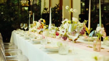 Pürüzsüz, yavaş çekim güzel dekore edilmiş uzun bir masa boyunca bir düğün resepsiyonu veya resmi bir ziyafet için hareket eder. Tabaklar, kristal bardaklar, pembe peçeteler ve...