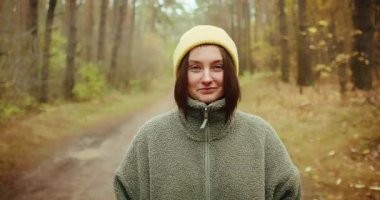 Kameraya bakıp gülümseyen mutlu bir genç kadının orta boy güzel bir portresi. Sarı bir bere ve rahat gri yün bir ceket giyiyor. Arka plan bulanık bir sonbahar.
