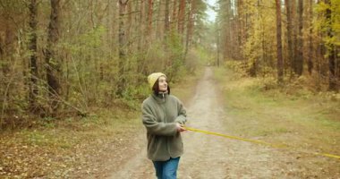 Sarı bereli ve tüylü ceketli genç bir kadının, tasmalı bir köpek ve güzel bir sonbahar ormanında yol alan başka bir köpeğin görüntüsü. Konsept