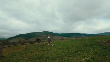 Steadicam ya da el bilgisayarı, iki enerjik Jack Russell teriyeri köpeğiyle manzaralı bir tepede yürürken genç bir kadını takip ediyor. Kırmızı kazaklı köpekler, devam ediyor.
