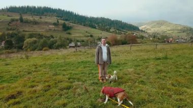 Steadicam ya da el bilgisayarı, iki enerjik Jack Russell teriyeri köpeğiyle manzaralı bir tepede yürürken genç bir kadını takip ediyor. Kırmızı kazaklı köpekler, devam ediyor.