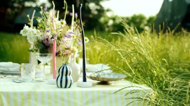 Sinematik bir çekim, güzel dekore edilmiş bir masa setini, kırsal bir düğün, brunch ya da akşam yemeği için yakalar. Masa, sarı ve beyaz çizgili bir masa örtüsüyle kaplı, uzun bir tarlada