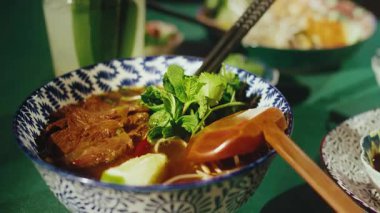 Güzel mavi beyaz bir seramik kasede servis edilen geleneksel Vietnamlı Pho Bo çorbasını yakından çek. Tabakta taze et dilimlenmiş pirinç eriştesi ve taze nane ile süslenmiş zengin et suyu var.