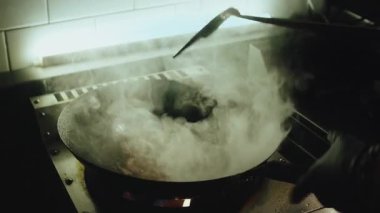 Profesyonel bir aşçının büyük bir ateş aleviyle tavada Asya yemeği pişirdiği bir film çekimi. Aşçı malzemeleri sıcak çelik bir tavaya atıyor ve bir restoran mutfağında alev etkisi yaratıyor. Yüksek