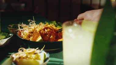 Asya restoranında lezzetli Pad Thai erişteleri yiyen aç bir insanı yakından çek. Bir erkek el, karidesli sıcak pirinç makarnasından büyük bir porsiyon koparmak için siyah çubuk kullanıyor.