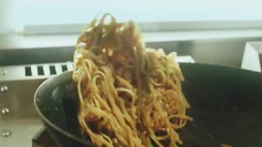 Siyah tavanın üstünde uçan lezzetli Pad Thai eriştelerinin yavaş çekim görüntüleri. Profesyonel bir aşçı lokanta mutfağında yemek pişirirken yemeği havaya fırlatıyor.