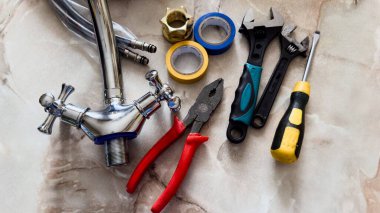 Karıştırıcı musluk pensesi, İngiliz anahtarı, teflon bant, esnek hortumlar ve taş bir yüzeye yeni bir krom musluk takmak için bir takım araçlar..