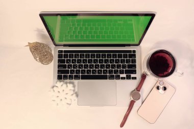 Şenlikli bir ortamda rahatlık ve teknoloji: yeşil ekran koruyuculu bir dizüstü bilgisayar, çay, cihazlar ve yeni yıl dekorasyonları kış içeriği, çevrimiçi selamlaşmalar, markalı görseller ve yaratıcı projeler için mükemmel bir zemin..