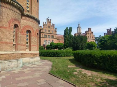 Chernivtsi Üniversitesi bahçesinde kubbeleri ve kuleleri olan tarihi tuğla binalar.