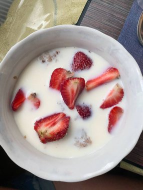 Sağlıklı kahvaltı kasesi çilek, tahıl gevreği ve dokulu sofra takımında süt.