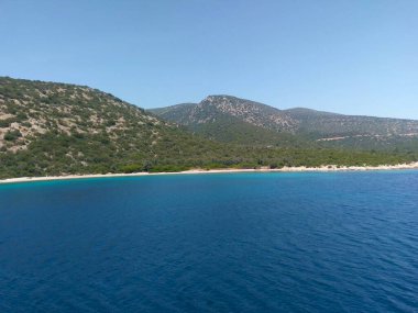 A deep blue bay with a sandy coastline and green hills under a clear sky in Bodrum