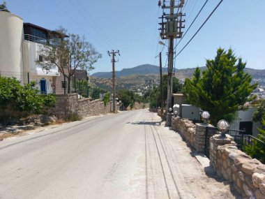 Bodrum 'da taştan çitler, beyaz binalar, yeşil ağaçlar ve arka planda tepeler olan sakin bir yerleşim yeri.