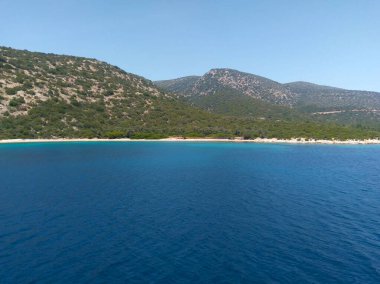 A deep blue bay with a sandy coastline and green hills under a clear sky in Bodrum
