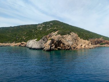 Turquoise water with a clear bottom, rocky coastline, and green hills in sunny Bodrum
