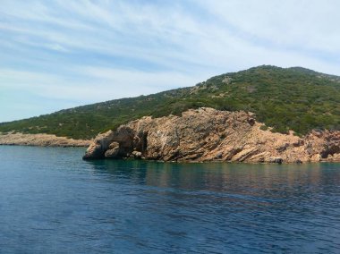 Turquoise water with a clear bottom, rocky coastline, and green hills in sunny Bodrum