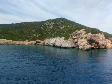Turquoise water with a clear bottom, rocky coastline, and green hills in sunny Bodrum
