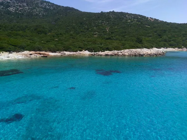 A yacht anchored in a crystal-clear turquoise bay with rocky shores and wooded hills in Bodrum, Turkey