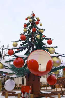 Karla kaplı bir tesiste kırmızı top koltuğu olan büyük bir Noel ağacı şeklinde şenlikli bir cazibe.