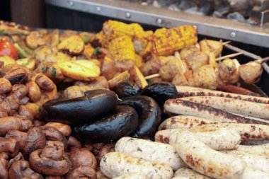 Bir sokak fuarında kızarmış sosis, mantar, mısır ve fırında patates ile çeşitli ızgara yemekler.