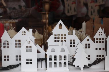 Beyaz ahşap evler ve Noel ağacı, kış dekorasyonu için sıcak mumlar sergilenen bir vitrinde.