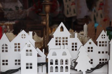 Beyaz ahşap evler ve Noel ağacı, kış dekorasyonu için sıcak mumlar sergilenen bir vitrinde.