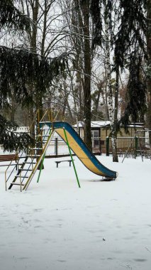 Karlı bir kış parkında parlak çocuklar kayıyor. Ayak izleri, çıplak ağaçlar ve yerleşim geçmişi var.