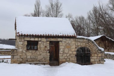 Kırsal taştan bir ev, karla kaplı bir çatı, ahşap kapılar, ve Kiev 'in açık hava müzesinin kış manzarasında kemerli bir uzantı..