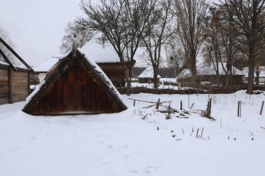 Kiev 'in açık hava müzesinde karla kaplı, dik çatılı, örülmüş çitleri ve kırsal kulübeleri olan geleneksel bir ahşap mahzen..