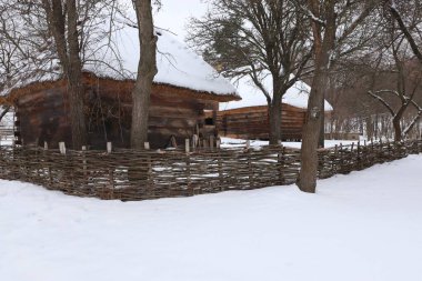 Kiev 'in açık hava müzesinin kış manzarasında sazdan çatıları, dokuma çitleri ve çıplak ağaçları olan karla kaplı ahşap kulübeler.