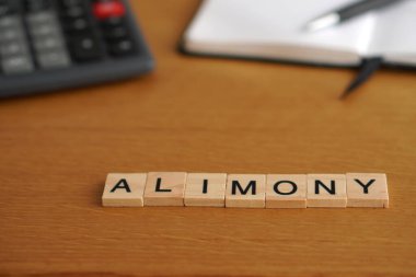 Nafaka. Finansal kavramlar. Arkaplanda hesap makinesi, defter ve kalem olan tahtadan harfler.