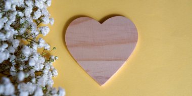 Sarı arka plan, beyaz bebek nefesli çiçekler ve kopya alanı olan tahta bir kalp.