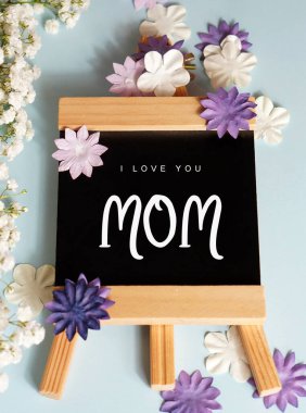 Seni seviyorum anne. Etrafında çiçekler olan bir tahtaya yazılmış kelimeler.