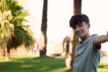 Küçük çocuk tatilinde palmiye ağaçlarıyla selfie çekiyor ve arka planda deniz var.