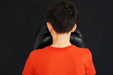Dövüş sanatları ve genç çocuklar. Sırtı kameraya dönük kırmızı tişört giyen ve arka planda boks eldivenli bir çocuk.
