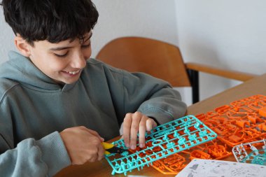 Ekransız boş zaman ve boş zaman. Manipülatif aktiviteler, iyi motor beceriler. Genç bir çocuk model yapmak için parça ve dişlileri ayırıyor.